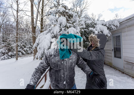 Two Yong Women In Winter Coats Playfully Push A Young Mans Face Into The Snow Stock Photo