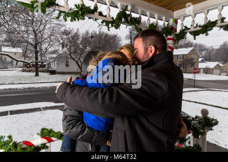 Two Caucasian Women And A Young Toddler Boy Stand On A Front Porch As It Snows Looking At The Christmas Decorations. Stock Photo