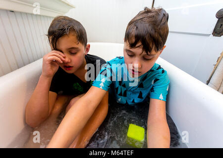 Twin Caucasian Brothers Play in Their Water Filled Bathtub Together With Their Clothes On Stock Photo