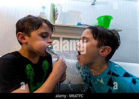 Twin Caucasian Brothers Play in Their Water Filled Bathtub Together With Their Clothes On Stock Photo