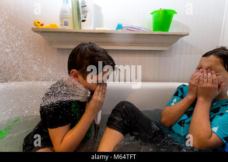 Twin Caucasian Brothers Play in Their Water Filled Bathtub Together With Their Clothes On Stock Photo