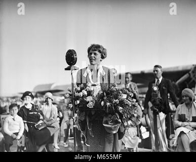 1920s 1929 AVIATOR AVIATRIX AMELIA EARHART SPEAKING TO CROWD HOLDING BOUQUET OF FLOWERS - asp gp74 ASP001 HARS B&W BLACK AND WHITE CAUCASIAN ETHNICITY EARHART GLENDALE AIRPORT JULY 7 OCCUPATIONS OLD FASHIONED PERSONS PUBLIC SPEAKING Stock Photo