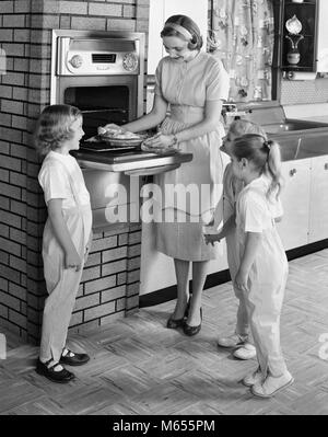 1950s MOTHER AND THREE DAUGHTERS STANDING AROUND OVEN IN KITCHEN BAKING PIE - asp x16744 CAM001 HARS HEALTHINESS HOME LIFE COPY SPACE FRIENDSHIP FULL-LENGTH LADIES DAUGHTERS INDOORS SIBLINGS CONFIDENCE SISTERS NOSTALGIA TOGETHERNESS 30-35 YEARS 35-40 YEARS 7-9 YEARS GOALS HOMEMAKER 5-6 YEARS HAPPINESS HOMEMAKERS BAKE MOMS AND HOUSEWIVES SIBLING COOPERATION SMALL GROUP OF PEOPLE JUVENILES MID-ADULT MID-ADULT WOMAN B&W BLACK AND WHITE CAUCASIAN ETHNICITY OLD FASHIONED PERSONS WALL OVEN Stock Photo