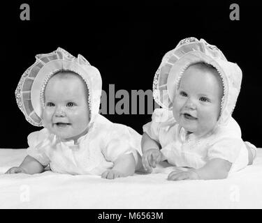 1950s TWIN BABY GIRLS WEARING BONNETS LYING ON THEIR STOMACHS SMILING - b4985 HAR001 HARS SIBLINGS CHUBBY SISTERS NOSTALGIA TOGETHERNESS 0-1 YEARS MATCHING SAME HAPPINESS HEAD AND SHOULDERS CHEERFUL GROWTH SIBLING SMILES JOYFUL LOOK-ALIKE 1-6 MONTHS BONNETS DUPLICATE JUVENILES LOOK ALIKE SIDE BY SIDE B&W BABY GIRL BLACK AND WHITE CAUCASIAN ETHNICITY CLONE OLD FASHIONED STOMACHS Stock Photo