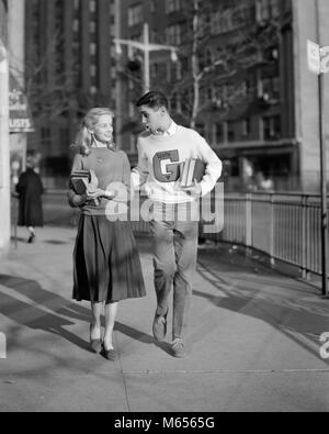1950s TEENAGE BOY WEARING VARSITY LETTER SWEATER WALKING GIRL HOME AFTER SCHOOL - bx018367 CAM001 HARS CLOTHING SWEATER NOSTALGIC PAIR ROMANCE FLIRTING BEAUTY STYLISH URBAN SIDEWALK OLD TIME FUTURE FLIRT OLD FASHION JUVENILE STYLE COMMUNICATION BLOND YOUNG ADULT BALANCE TWO PEOPLE CAUCASIAN PLEASED JOY LIFESTYLE FEMALES HEALTHINESS COPY SPACE FRIENDSHIP FULL-LENGTH LADIES CARING TEENAGE GIRL TEENAGE BOY COUPLES SERENITY CONFIDENCE NOSTALGIA TOGETHERNESS TEMPTATION HAPPINESS WELLNESS LEISURE PROTECTION STYLES UNIVERSITIES CHOICE 18-19 YEARS SUPPORT GROWTH HIGH SCHOOL SMILES VARSITY CONNECTION Stock Photo