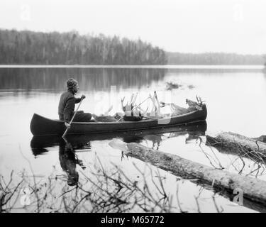 1920s MAN HUNTING GUIDE PADDLING CANOE IN LAKE CARRYING MOOSE AND DEER CARCASSES - h97 HAR001 HARS RECREATION DIRECTION ISOLATED MASCULINE WILDERNESS SEASON GUIDE SOLITARY HUNTERS MALES MID-ADULT MID-ADULT MAN PADDLING PRIMITIVE REMOTE SEASONAL WILDLIFE B&W BLACK AND WHITE CARCASS DEER MOOSE OLD FASHIONED PERSONS Stock Photo