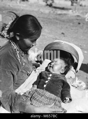 1930s NATIVE AMERICAN NAVAJO INDIAN WOMAN MOTHER HOLDING SMILING BABY PAPOOSE IN CRADLE BOARD - i1125 HAR001 HARS NORTH AMERICA TOGETHERNESS 20-25 YEARS NORTH AMERICAN HAPPINESS HIGH ANGLE 18-19 YEARS GROWTH PAPOOSE NATIVE AMERICAN SOUTHWEST 1-6 MONTHS YOUNG ADULT WOMAN B&W BABY GIRL BLACK AND WHITE CHILD CARRIER CRADLE BOARD CRADLE BOARDS INDIGENOUS OLD FASHIONED SOUTHWESTERN Stock Photo