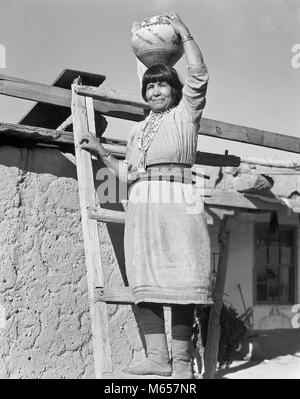 1930s NATIVE AMERICAN INDIAN WOMAN STANDING ON LADDER HOLDING OLLA WATER JAR POTTERY ON HER HEAD COCHITI PUEBLO NEW MEXICO USA - i1694 HAR001 HARS INDIANS UNITED STATES OF AMERICA NOSTALGIA POTTERY MIDDLE-AGED JAR EYE CONTACT 40-45 YEARS 45-50 YEARS SINGLE OBJECT MIDDLE-AGED WOMAN BEAD PRIDE NATIVE AMERICAN PUEBLO COCHITI NATIVE AMERICANS NEW MEXICO B&W BLACK AND WHITE LOOKING AT CAMERA OLD FASHIONED OLLA PERSONS Stock Photo