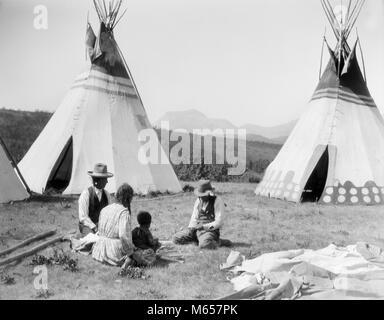 1920s NATIVE AMERICAN INDIAN FAMILY MAN WOMAN TWO CHILDREN SITTING IN FRONT OF TEPEES SIOUX TRIBE MONTANA USA - i354 HAR001 HARS OLD TIME OLD FASHION JUVENILE STYLE MONTANA SONS LIFESTYLE HISTORY FEMALES LODGE RURAL HOME LIFE UNITED STATES FULL-LENGTH LADIES INDIANS UNITED STATES OF AMERICA SIOUX COUPLES SPIRITUALITY NOSTALGIA FATHERS SHELTER NORTH AMERICA TOGETHERNESS 3-4 YEARS 30-35 YEARS 35-40 YEARS FREEDOM HISTORIC NORTH AMERICAN 5-6 YEARS TEEPEE MOMS TIPI DADS EXTERIOR PRIDE TEPEE TRIBE MT GROUP OF PEOPLE NATIVE AMERICAN JUVENILES MALES MID-ADULT MID-ADULT MAN MID-ADULT WOMAN TEPEES B&W Stock Photo