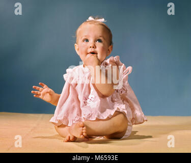 1960s LITTLE BABY GIRL SITTING WEARING PINK DRESS AND WHITE HAIR RIBBON LOOKING UPWARD - kb6262 HAR001 HARS 1-2 YEARS HAPPINESS EXCITEMENT GROWTH PEOPLE BABIES 6-12 MONTHS HAIR RIBBON JUVENILES LOOKING UP UPWARD BABY GIRL CAUCASIAN ETHNICITY HAND TO MOUTH LOOKING AT CAMERA OLD FASHIONED PINK DRESS Stock Photo