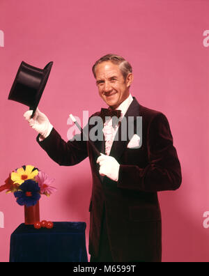 1970s MAN MAGICIAN LOOKING AT CAMERA TIPPING TOP HAT WITH WHITE GLOVES BOW TIE MAGIC WAND FLOWERS - kc6296 HAR001 HARS STUDIO SHOT GROWNUP ONE PERSON ONLY COPY SPACE HALF-LENGTH GROWN-UP CHARACTER INDOORS PROFESSION ENTERTAINMENT CONFIDENCE NOSTALGIA MIDDLE-AGED MIDDLE-AGED MAN EYE CONTACT 40-45 YEARS 45-50 YEARS PERFORMING ARTS PEOPLE STORY OCCUPATION HAPPINESS WAND PERFORMER CAREERS CHARACTERS EXCITEMENT ENTERTAINER SMILES JOYFUL ACTORS IMAGINATION PERFORMERS ENTERTAINERS HEAD-WARE MAGICAL WHITE GLOVES MALES TOP HAT CAUCASIAN ETHNICITY LOOKING AT CAMERA OCCUPATIONS OLD FASHIONED ON STAGE Stock Photo