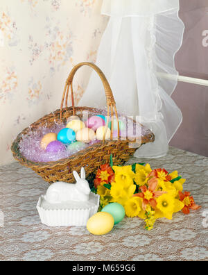 1970s BASKET FULL OF PASTEL DYED EASTER EGGS ON TABLE TOP BY WINDOW BOUQUET OF DAFFODILS MILK GLASS RABBIT DISH - ke1419 HAR001 HARS DYED OLD FASHIONED SHEER TABLE TOP Stock Photo