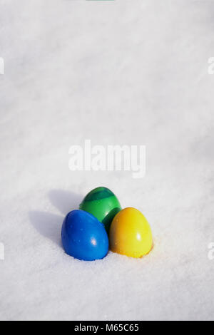 three easter eggs painted in vibrant colors in fresh snow Stock Photo