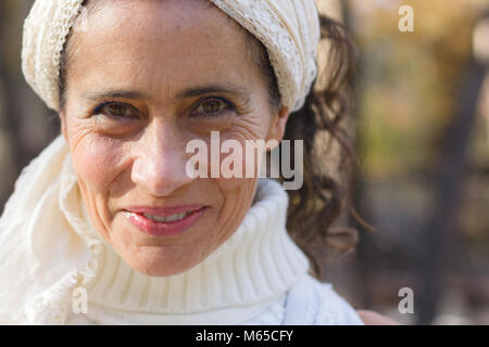 Close up on confident mature woman smiling with white turtle neck knitted sweater and shawl on head Stock Photo
