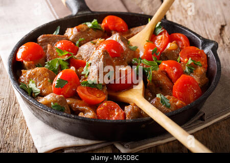 Stewed beef in spicy sauce with tomatoes and greens close-up on a pan. horizontal Stock Photo