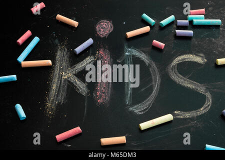 Group of multicolored chalks on black chalkboard with word "kids" written on it. Stock Photo