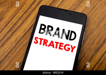 Word, writing handwriting Brand Strategy. Business concept for Marketing Idea Plan Written on mobile phone, wooden background with copy space. Stock Photo