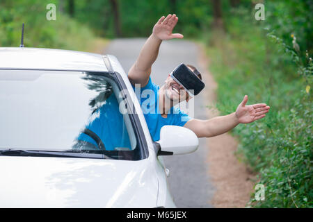 Portrait of young man using virtual reality glasses through car window with hands up. Road in the background. Stock Photo