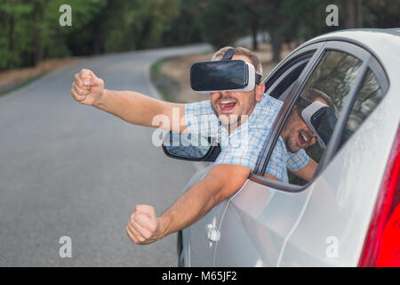 Portrait of young man using virtual reality glasses through car window. Road in the background. Space for copy. Stock Photo