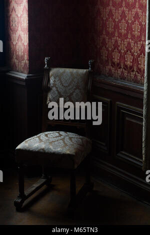 side view of antique armchair in the corner of a classical style room with vintage red wall paper natural lightning Stock Photo
