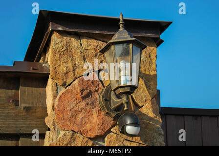 Street lamp in retro style, with a light sensor, on a pillar made of natural stone. Against the blue sky. Lighting in the village. Stock Photo