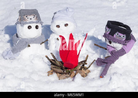 Cute little snowmen dressed for winter, huddled around a fire trying to keep warm. Snow covered scene in Norfolk UK Stock Photo