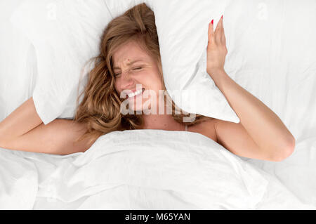 Too much noise. Woman in bed covering ears with pillow because of noise. Stock Photo