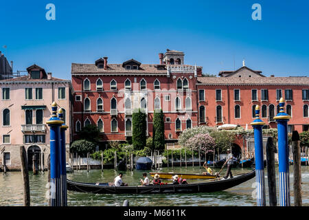 Gondolier riding his gondola, taking tourists for a Grand Canal city sightseeing tour. Magical Venice, Italy, Europe, EU. Clear blue sky, copy space. Stock Photo