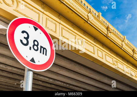 Circular low bridge regulatory road sign with red ring showing the height limit on non-arch yellow bridge against blue sky Stock Photo