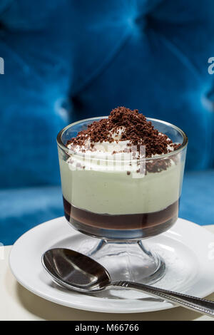 Grasshopper Icebox Cake with crumbles in a Dessert cup on a plate at a Diner restaurant table with spoon and blue velvet seat cushion background Stock Photo