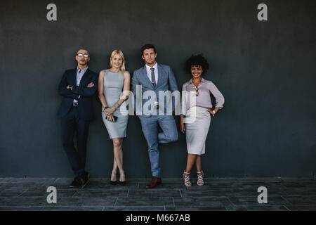 Full length portrait of diverse business team standing together against a wall. Group of business men and women looking at camera. Stock Photo