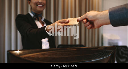 Close up of businessman paying with credit card at reception desk in hotel. Business man giving credit card to hotel receptionist for payment of his r Stock Photo