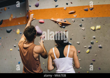 Rear view of male instructor giving instructions to a woman on wall climbing. Woman learning the art of rock climbing at an indoor climbing centre. Stock Photo
