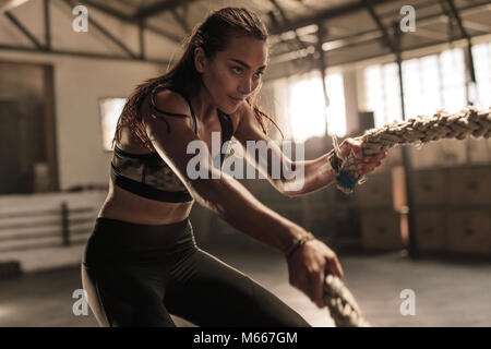 fitness woman using battle ropes for exercising. Female working out with battle ropes at cross gym. Stock Photo