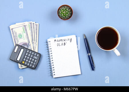 Notepad with pen, coffee, dollars, calculator and cactus on a blue background. Copy the space. Top view. Financial, marketing, business plan Stock Photo
