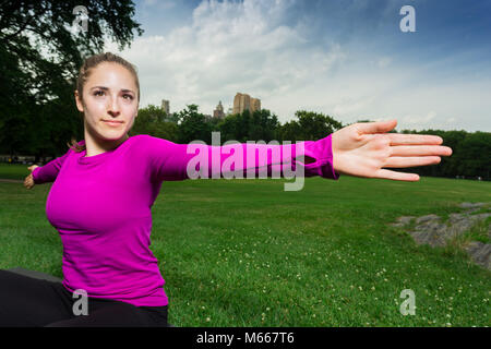 Young Caucasian Woman Practices Yoga In Central Park NYC While Wearing A Magenta Top, Black Leggings and Barefoot Stock Photo
