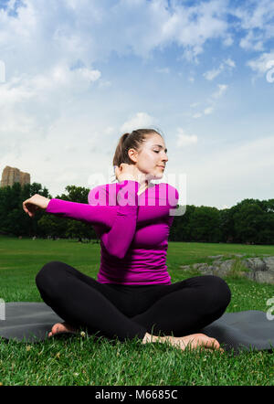 Young Caucasian Woman Practices Yoga In Central Park NYC While Wearing A Magenta Top, Black Leggings and Barefoot Stock Photo