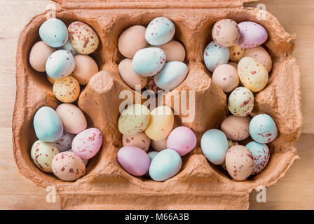 Overhead view of an opened brown egg carton, filled with piles of small egg shaped Easter sweets. Stock Photo