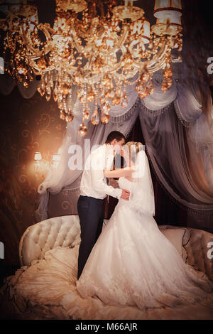 Happy groom and the bride stand on a bed in a bedroom or in a hotel room Stock Photo