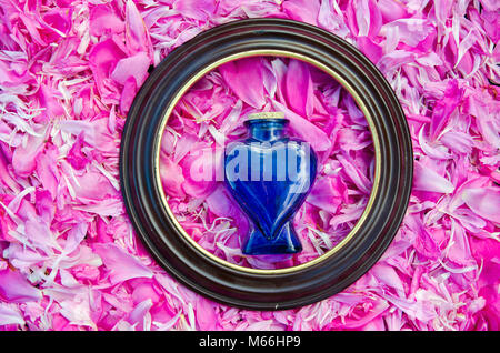 Round frame and vintage perfume scent blue heart form bottle on fresh peony petals background Stock Photo