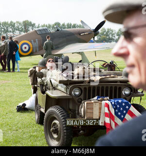 Willis jeep with American flag on airfield with RAF spitfire plane in the background on location at the Goodwood revival event in sussex Stock Photo