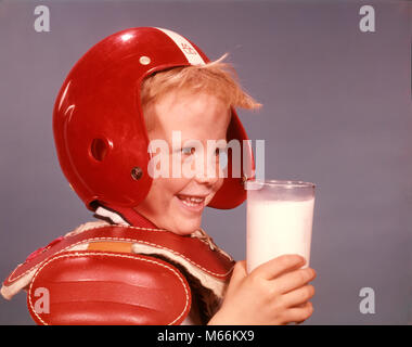 1960s SMILING BLOND BOY RED PLASTIC FOOTBALL HELMET SHOULDER PADS HOLDING GLASS OF MILK - kf3290 HAR001 HARS INDOORS NOSTALGIA 5-6 YEARS HAPPINESS WELLNESS HEAD AND SHOULDERS NOURISH BEVERAGE PROTECTION STRENGTH FLUID NUTRITION RECREATION GROWTH ATHLETES NOURISHMENT BALL SPORT JUVENILES MALES SHOULDER PADS AMERICAN FOOTBALL CAUCASIAN ETHNICITY DAIRY PRODUCT GLASS OF MILK OLD FASHIONED Stock Photo