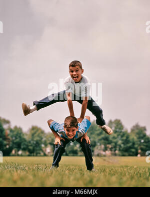 1960s BOYS PLAYING LEAP FROG ONE JUMPING OVER THE OTHER'S BACK LOOKING AT CAMERA - kj3099 HAR001 HARS HOME LIFE ATHLETICS COPY SPACE FRIENDSHIP HALF-LENGTH ATHLETIC SIBLINGS CONFIDENCE NOSTALGIA TOGETHERNESS EYE CONTACT 10-12 YEARS FREEDOM SUCCESS HAPPINESS EXCITEMENT LOW ANGLE GROWTH SIBLING JOYFUL ATHLETES BLUE JEANS JUVENILES MALES PRE-TEEN PRE-TEEN BOY CAUCASIAN ETHNICITY LEAP FROG LOOKING AT CAMERA OLD FASHIONED OTHER' Stock Photo