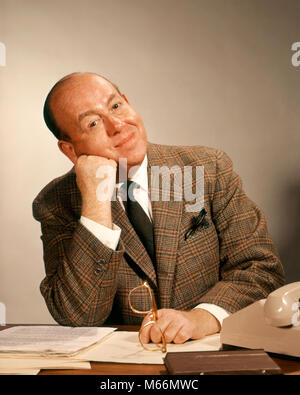 1960s BUSINESSMAN AT OFFICE DESK HAND TO FACE HEAD TILTED LEANING ON FIST LOOKING AT CAMERA - kp1310 HAR001 HARS COMMUNICATION CAREER PEACE SIGNAL CAUCASIAN TIRED PLEASED LIFESTYLE SATISFACTION STUDIO SHOT PORTRAITS ONE PERSON ONLY COMMUNICATING COPY SPACE HALF-LENGTH INDOORS PLAID PROFESSION EYEGLASSES NOSTALGIA MIDDLE-AGED MIDDLE-AGED MAN WORK PLACE EYE CONTACT 40-45 YEARS 45-50 YEARS WHITE COLLAR SUIT AND TIE DREAMS OCCUPATION SELLING SATISFIED BALDING LEADERSHIP OCCASION COMMUNICATE TILTED SALESMEN MALES PEOPLE ADULTS CAUCASIAN ETHNICITY EASY GOING LOOKING AT CAMERA OCCUPATIONS Stock Photo