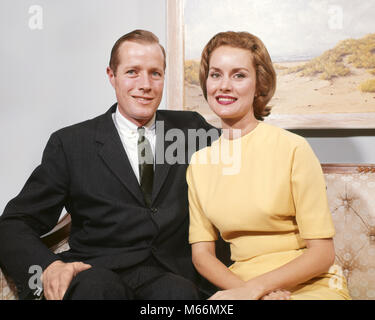 1960s HAPPY COUPLE SITTING ON SOFA MAN WEARING BUSINESS SUIT TIE WOMAN IN A YELLOW DRESS LOOKING AT CAMERA SMILING - kp604 HAR001 HARS LIFESTYLE FEMALES MARRIED STUDIO SHOT PORTRAITS SPOUSE HUSBANDS GROWNUP HOME LIFE COPY SPACE FRIENDSHIP HALF-LENGTH LADIES GROWN-UP COUPLES INDOORS PROFESSION CONFIDENCE NOSTALGIA TOGETHERNESS EYE CONTACT 25-30 YEARS 30-35 YEARS SUIT AND TIE WIVES HAPPINESS OCCASION SMILES JOYFUL COOPERATION MALES MID-ADULT MID-ADULT MAN MID-ADULT WOMAN PEOPLE ADULTS CAUCASIAN ETHNICITY LOOKING AT CAMERA OLD FASHIONED PERSONS Stock Photo