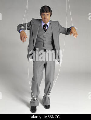 1970s BUSINESSMAN SUSPENDED ON PUPPET STRINGS LOOKING AT CAMERA - ks15206 HAR001 HARS POLITICS CONNECTION THREE PIECE SUIT WACKY SALESMEN SYMBOLIC HELPLESS MALES MANIPULATED MID-ADULT MID-ADULT MAN CAUCASIAN ETHNICITY CONTROLLED DANGLING DOMINATED DUPE LIMITATION LIMITS LOOKING AT CAMERA MANIPULATION MINION OCCUPATIONS OLD FASHIONED PAWN PERSONS POWERLESS RESTRAINED RESTRICT RESTRICTED STOOGE SUPERVISED SUSPENDED TIED BY VULNERABLE Stock Photo