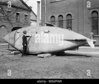 1930s MAN STANDING NEXT TO OLD SUBMARINE FROM 1864 THE INTELLIGENT WHALE BROOKLYN NAVY YARD NEW YORK CITY USA - q37778 CPC001 HARS NYC HIGH TECH NEW YORK CITIES NEW JERSEY NEW YORK CITY BOROUGH MALES 1864 AMERICAN CIVIL WAR B&W BIG APPLE BLACK AND WHITE BROOKLYN NAVY YARD INTELLIGENT WHALE MILITIA MUSEUM OF NEW JERSEY NATIONAL GUARD ODDITY OLD FASHIONED PERSONS SEA GIRT WHALE SHAPE Stock Photo