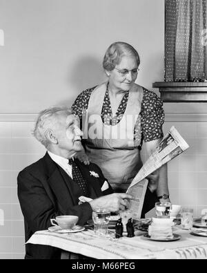 1940s ELDERLY COUPLE MAN WOMAN IN KITCHEN MAN SITTING AT TABLE WOMAN LOOKING OVER HIS SHOULDER READING NEWSPAPER - r13244 HAR001 HARS CAUCASIAN PLEASED JOY ELDER FEMALES MARRIED STUDIO SHOT SPOUSE HUSBANDS HEALTHINESS HOME LIFE COPY SPACE FRIENDSHIP HALF-LENGTH LADIES CARING NEWSPAPERS COUPLES INDOORS RETIREMENT SENIOR MAN SENIOR ADULT NOSTALGIA MORNING TOGETHERNESS SENIOR WOMAN HOMEMAKER WIVES HOMEMAKERS OLDSTERS CHEERFUL OLDSTER HIS HOUSEWIVES SMILES ELDERS JOYFUL 70s ADULT ELDERLY MAN 80-PLUS ADULT ELDERLY WOMAN MALES B&W BLACK AND WHITE CAUCASIAN ETHNICITY HOME MAKER HOUSE WIFE HOUSEKEEPER Stock Photo