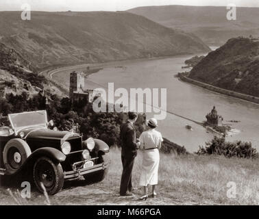 1930s COUPLE WITH TOURING CAR OVERLOOKING RHINE RIVER BURG GUTENFELS AND CASTLE PFALZGRAFENSTEIN ON FALKENAU ISLAND GERMANY - r390 HAR001 HARS TRANSPORTATION NOSTALGIA EUROPE TOGETHERNESS 25-30 YEARS 30-35 YEARS 35-40 YEARS TOUR WIVES HIGH ANGLE ADVENTURE LEISURE RELAXATION AUTOS KNOWLEDGE TOURIST HOLDING HANDS TOURISTS AUTOMOBILES VEHICLES CASTLES MALES MID-ADULT MID-ADULT MAN MID-ADULT WOMAN PACKARD B&W BLACK AND WHITE BURG GUTENFELS CASTLE KAUB CAUCASIAN ETHNICITY FALKENAU ISLAND FALZ CASTLE OLD FASHIONED ON THE RHINE PERSONS PFALZGRAFENSTEIN TOURING TOURISM Stock Photo
