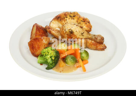 Roasted poussin chicken with roast potatoes vegetables and gravy on a plate isolated against white Stock Photo